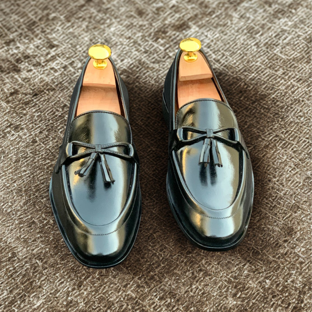 "Pair of elegant black leather tassel loafers with polished finish and wooden shoe trees on dark background"
