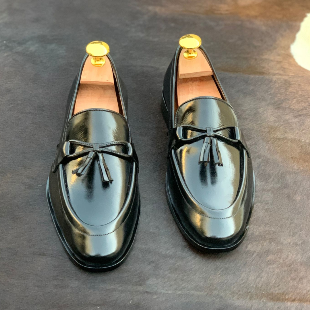 "Pair of elegant black leather tassel loafers with polished finish and wooden shoe trees on dark background"